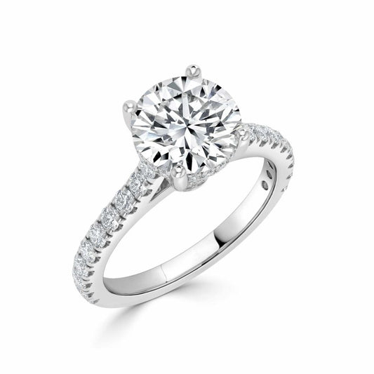 A round-cut diamond solitaire engagement ring with a pavé-set diamond band in a silver-colored metal, shown on a clean white background.