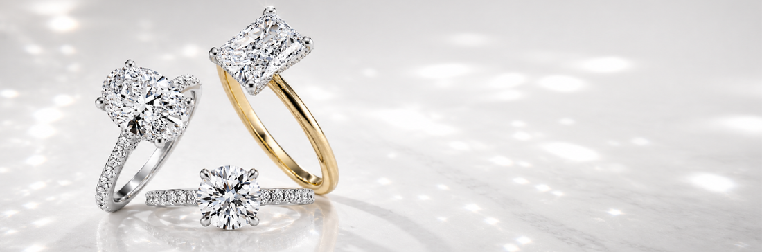 Three diamond engagement rings showcasing different carat sizes and cuts — cushion, round brilliant, and halo — in white and yellow gold settings on a bright reflective surface.