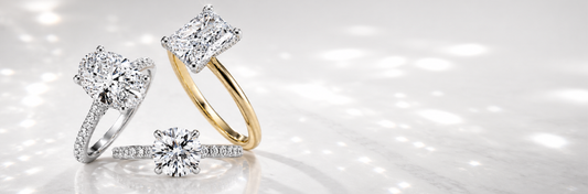 Three diamond engagement rings showcasing different carat sizes and cuts — cushion, round brilliant, and halo — in white and yellow gold settings on a bright reflective surface.