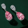 A pair of high-end drop earrings featuring large, sparkling pink diamonds in teardrop-shaped settings, suspended from silver-toned hoops with smaller clear diamonds, set against a dark green background.