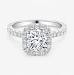 A cushion cut diamond halo ring in white gold or platinum, featuring a large cushion-cut center diamond surrounded by a halo and a pavé-set band, shown on a light gray background.
