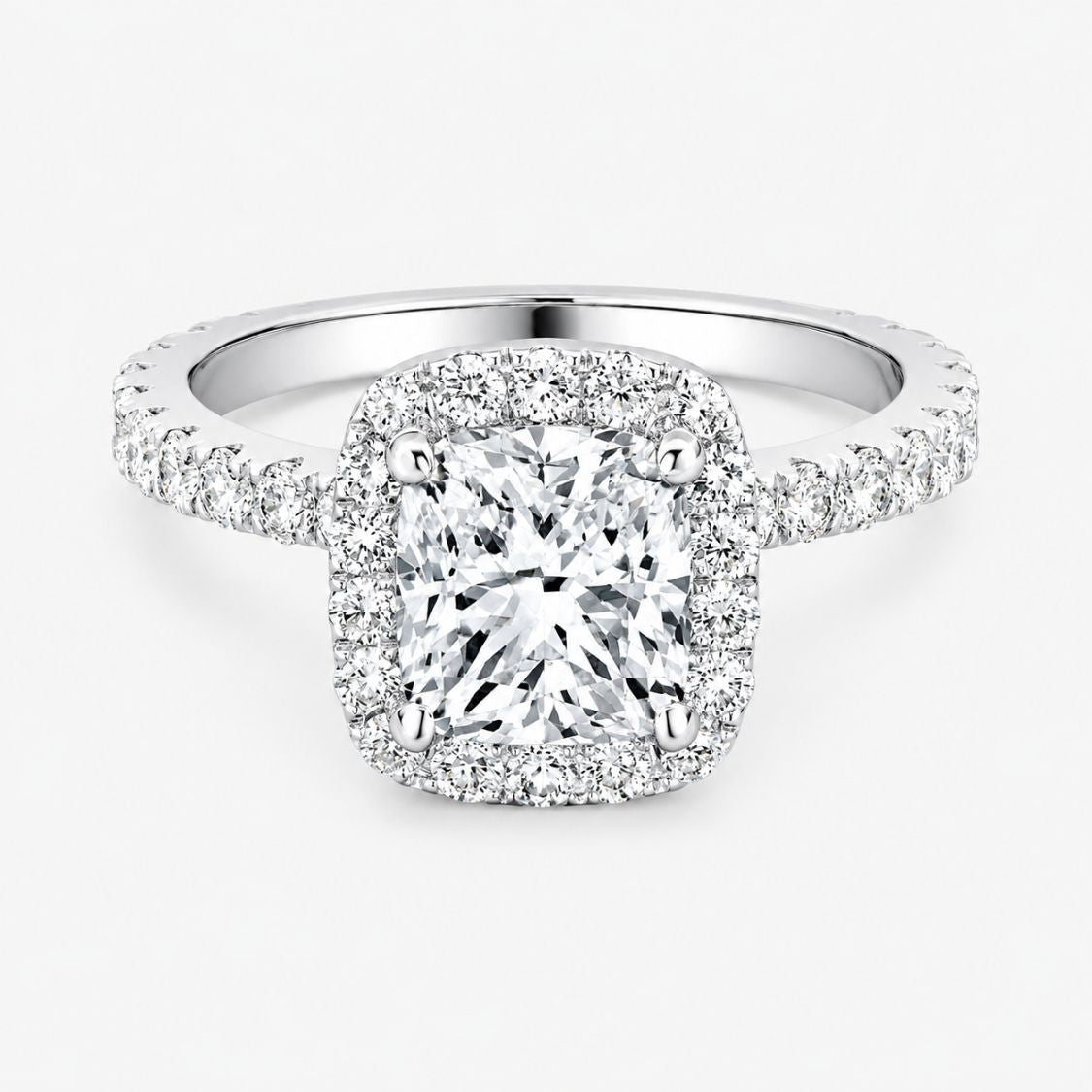 A cushion cut diamond halo ring in white gold or platinum, featuring a large cushion-cut center diamond surrounded by a halo and a pavé-set band, shown on a light gray background.