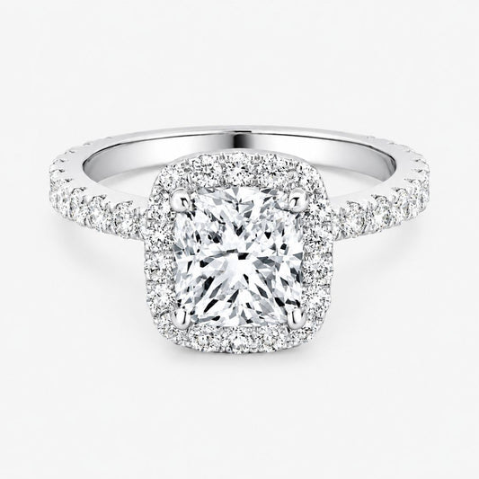 A cushion cut diamond halo ring in white gold or platinum, featuring a large cushion-cut center diamond surrounded by a halo and a pavé-set band, shown on a light gray background.