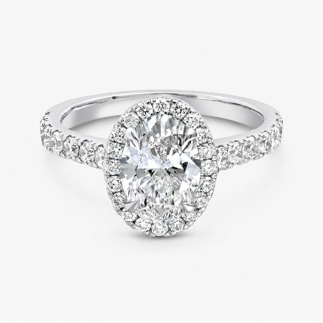 An oval halo engagement ring featuring a large round-cut center stone surrounded by a double halo of smaller stones, set on a split-shank band with pavé accents, in a polished silver-toned metal against a light gray background.