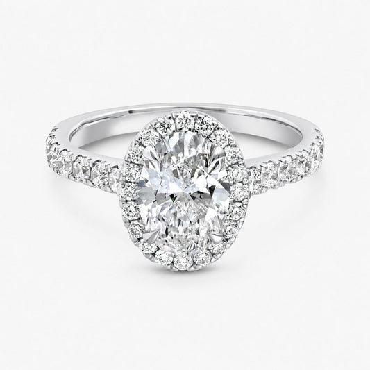 An oval halo engagement ring featuring a large round-cut center stone surrounded by a double halo of smaller stones, set on a split-shank band with pavé accents, in a polished silver-toned metal against a light gray background.