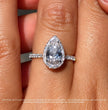 A close-up of a hand wearing a white gold ring with a teardrop-shaped clear center stone surrounded by a halo, with small side stones on the band.