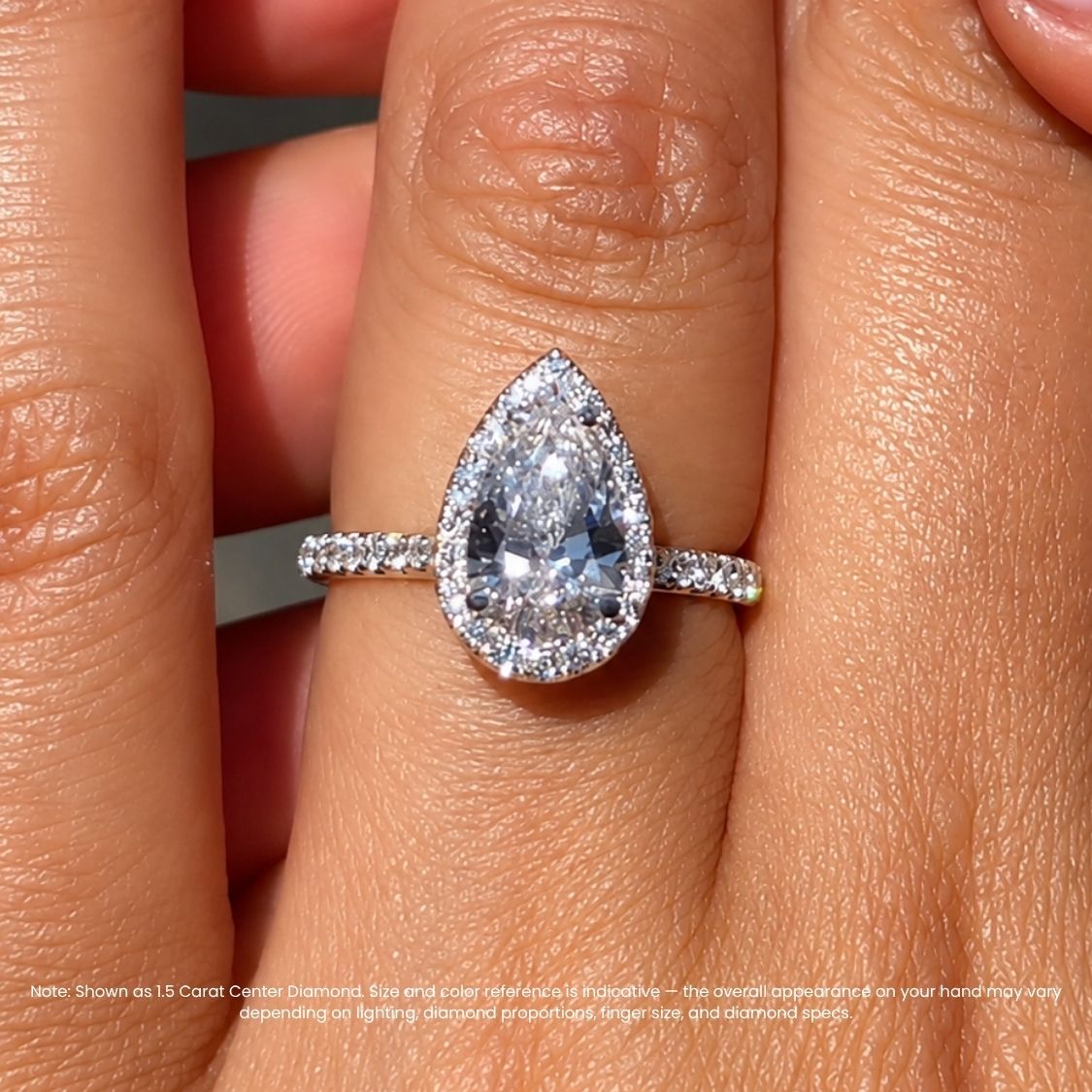 A close-up of a hand wearing a white gold ring with a teardrop-shaped clear center stone surrounded by a halo, with small side stones on the band.