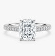 An engagement ring featuring a large rectangular cushion-cut center diamond in a four-prong setting, with a polished silver-colored band adorned with pavé diamonds on each side, set against a clean white background.