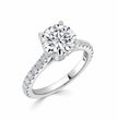 A round-cut diamond solitaire engagement ring with a pavé-set diamond band in a silver-colored metal, shown on a clean white background.