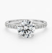 A round-cut diamond solitaire engagement ring with a pavé-set diamond band in a silver-colored metal, shown on a clean white background.