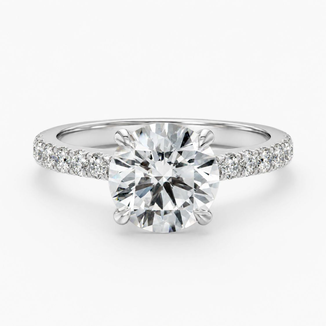 A round-cut diamond solitaire engagement ring with a pavé-set diamond band in a silver-colored metal, shown on a clean white background.