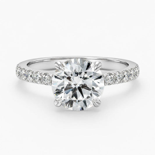 A round-cut diamond solitaire engagement ring with a pavé-set diamond band in a silver-colored metal, shown on a clean white background.