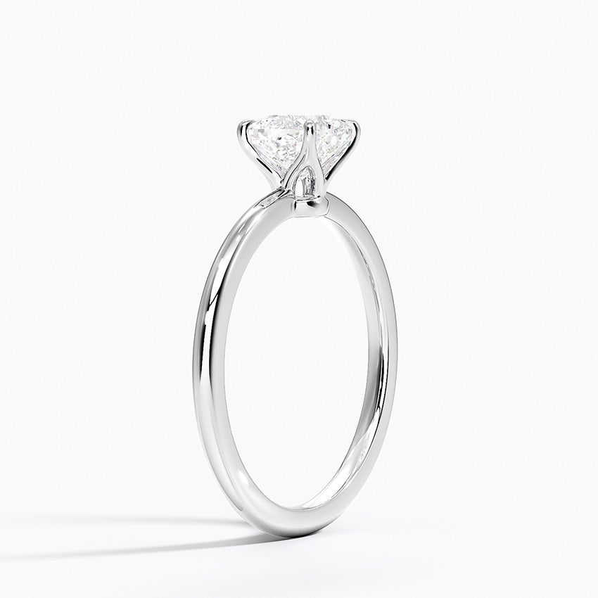 Side view of a platinum solitaire cushion cut engagement ring with prong setting on white background